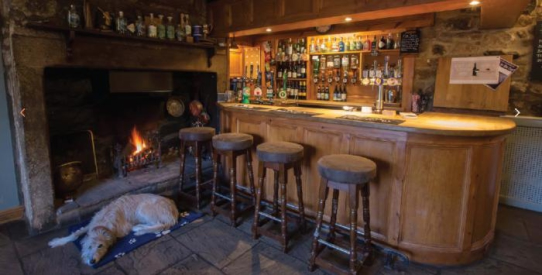 A pub bar area with a log burning fire and a dog relaxing next to the fire
