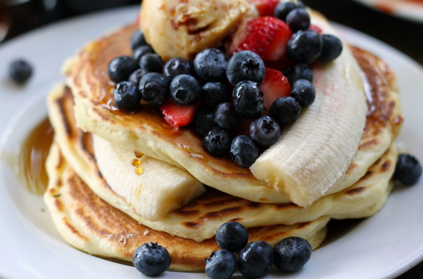 A stack of pancakes with blueberries, strawberries and a banana on top
