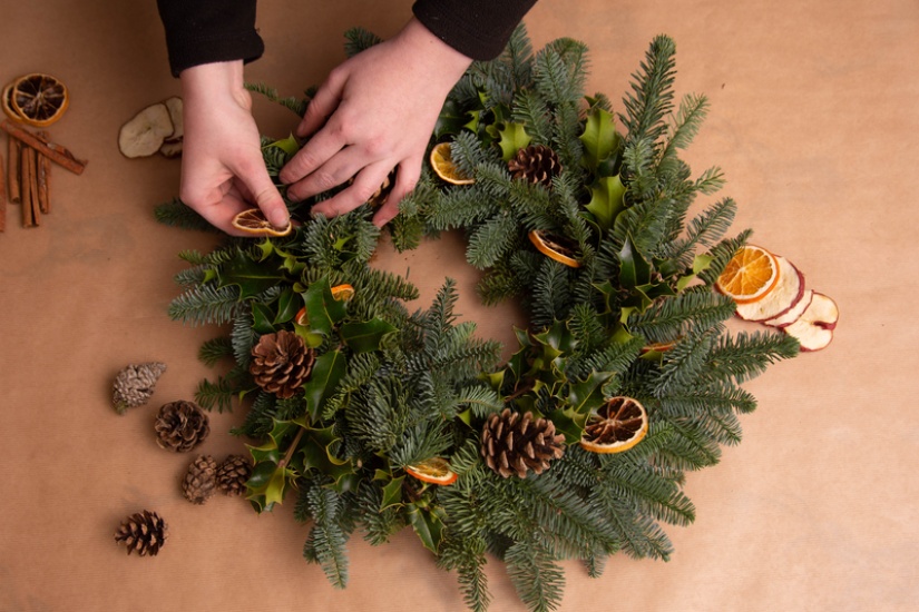 A person's hands putting a dried orange slice on a circular wreath