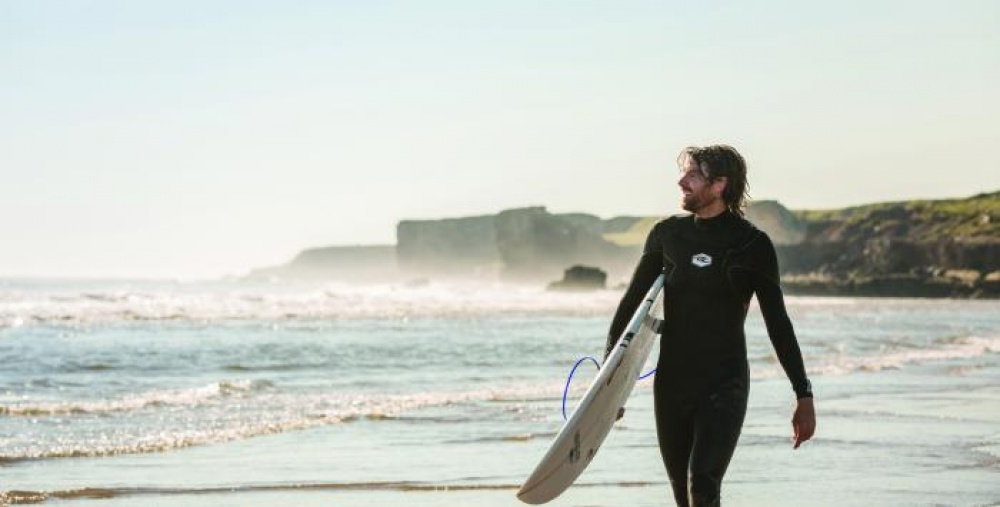 Surfer in black wetsuit holding a surf board on the beach