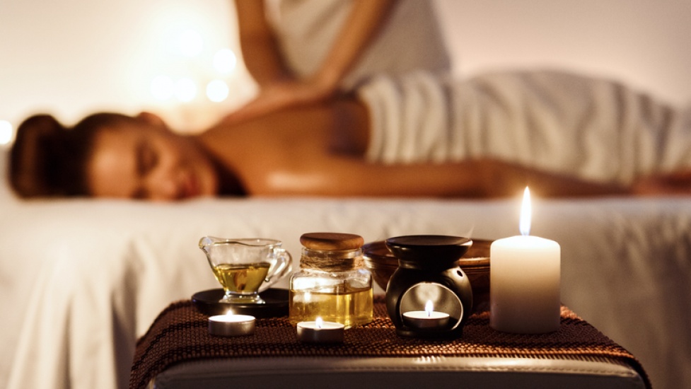 Relaxed woman enjoying aromatherapy massage in luxury spa with candle on foreground