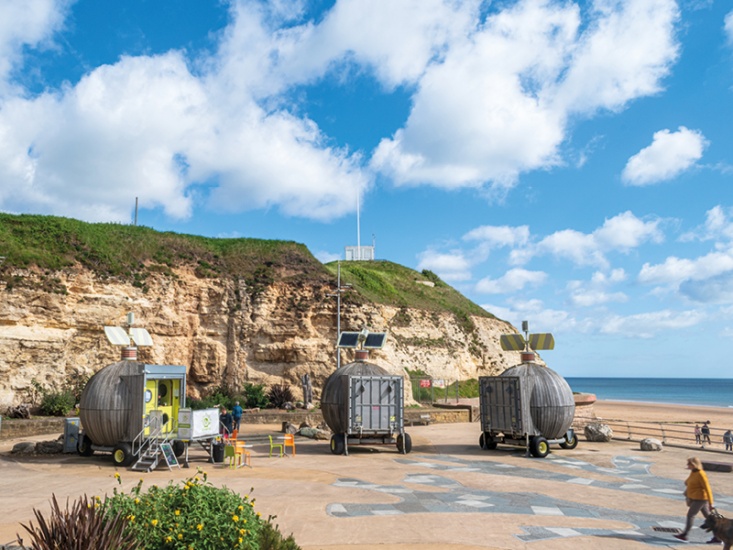 Metal pods on wheels beside the beach and Cliffside