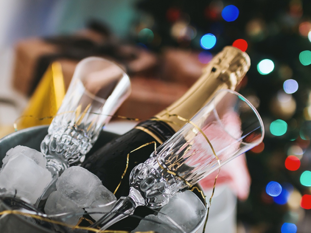 2 glass flutes and a bottle of champagne in an ice butter with colourful lights blurred in the background