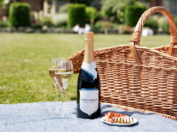 2 glasses of sparkling English white on a picnic blanket with a basket