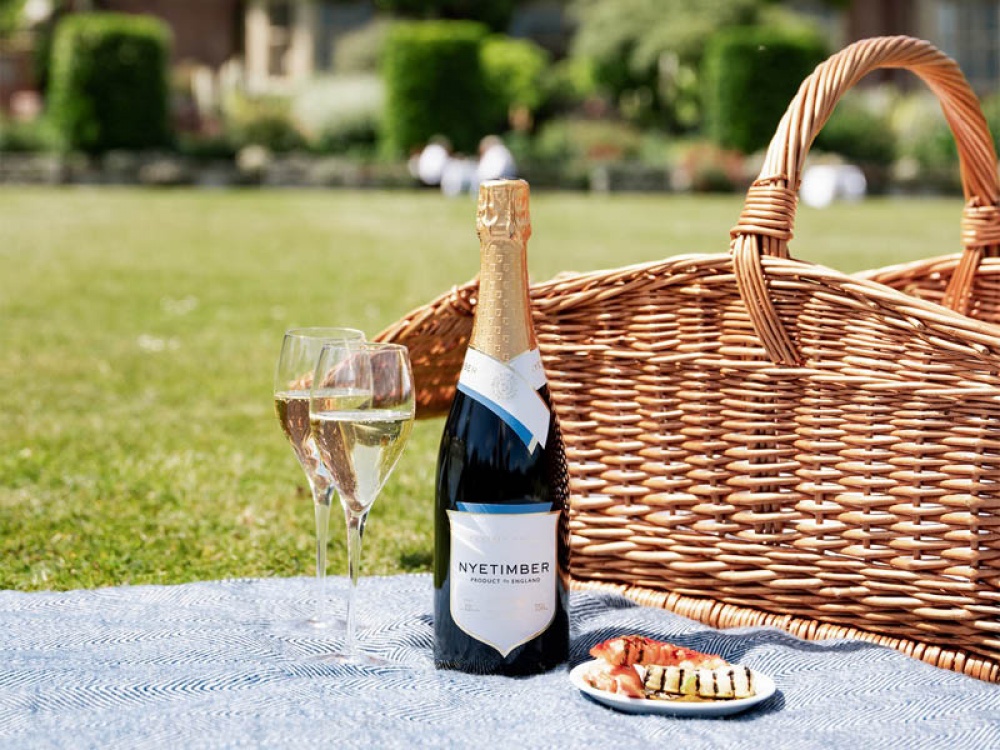 2 glasses of sparkling English white on a picnic blanket with a basket