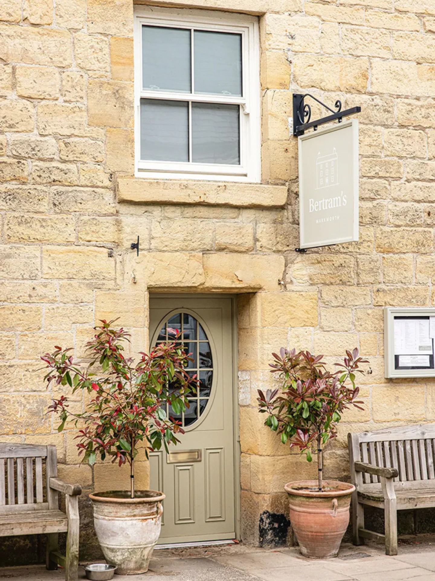 stone built building with a green door and 2 small tree planters