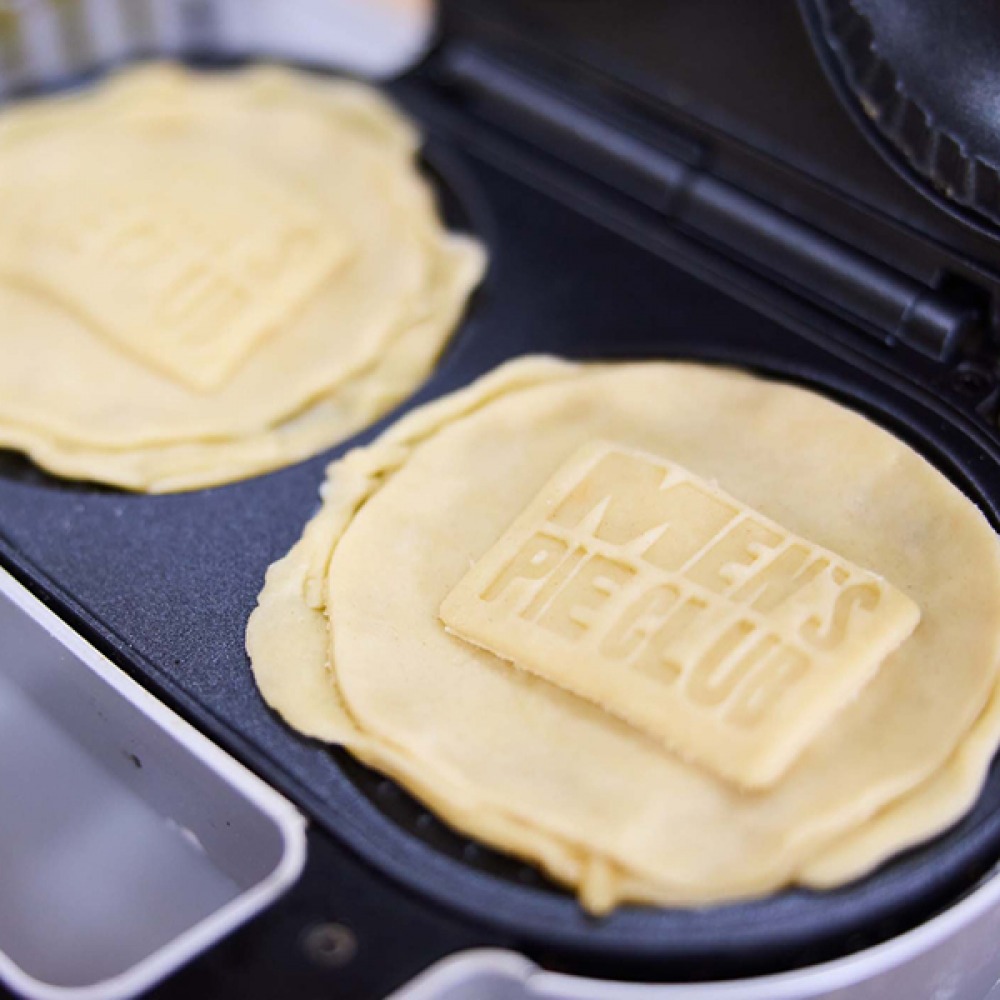 'Mens Pie Club' stamped into pastry on top of pies sitting in pie maker