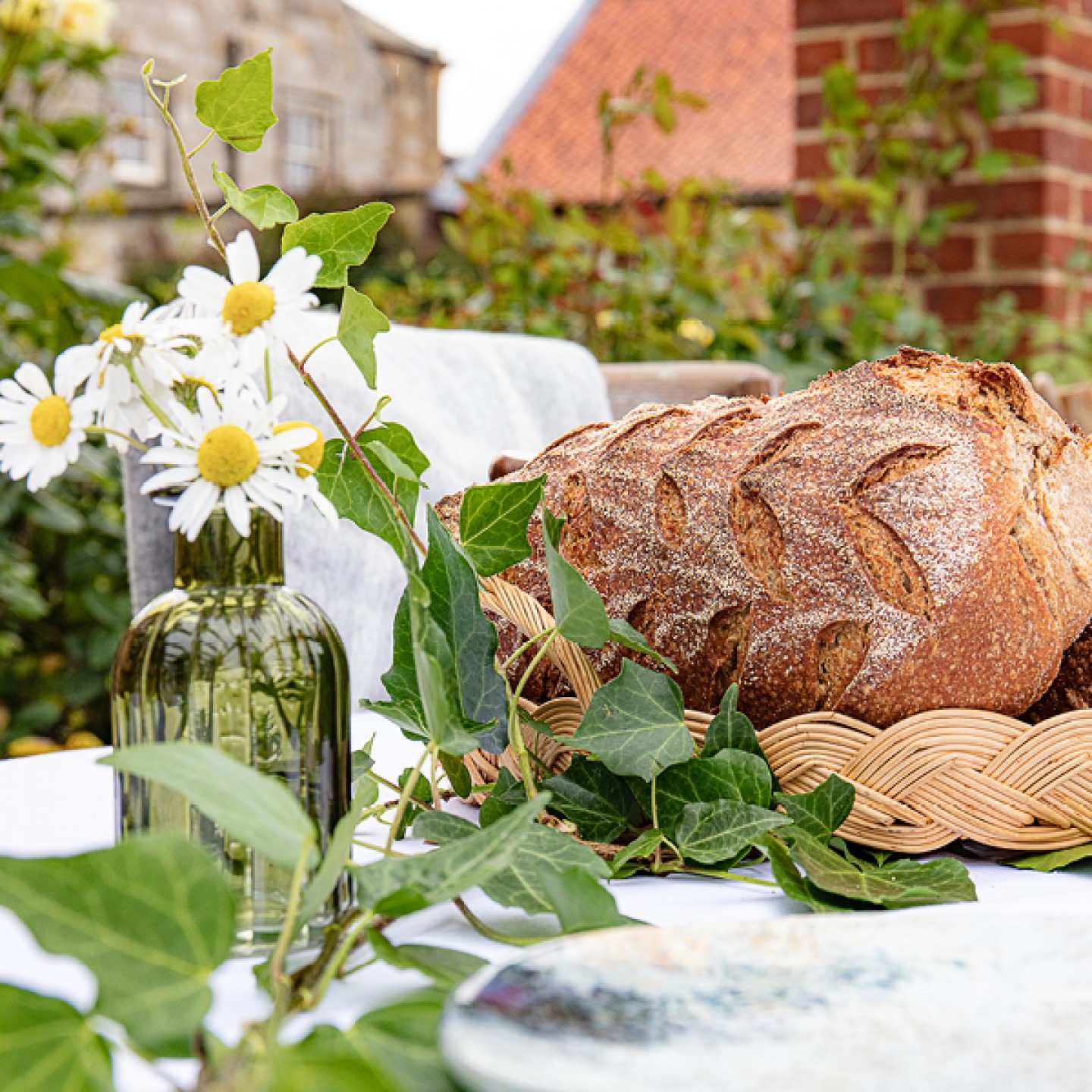 fresh crusty bread on a wicker tray with daisy's in glass vase