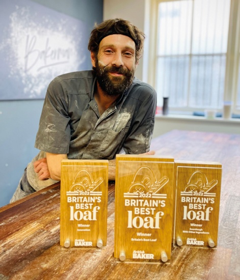 Dan Booth covered in flour standing in front of Britains Best Loaf Award