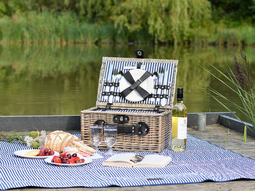 picnic basket set with food and wine by a lake