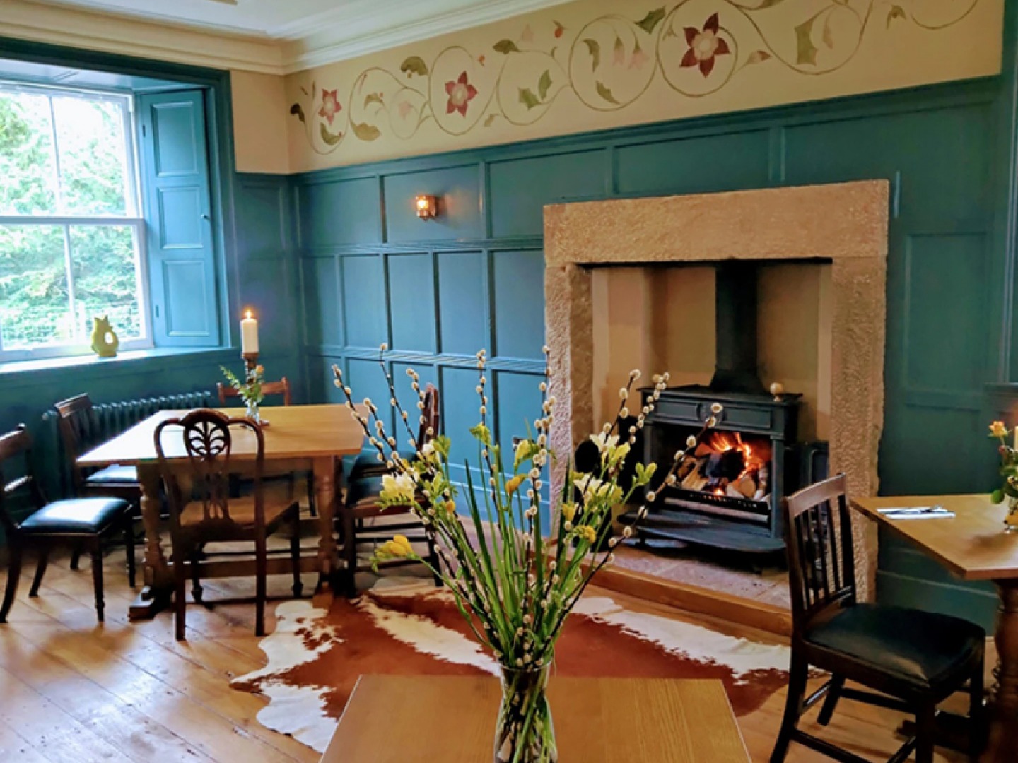 Three tables in front of a fire with a vase with flowers in as a focal point