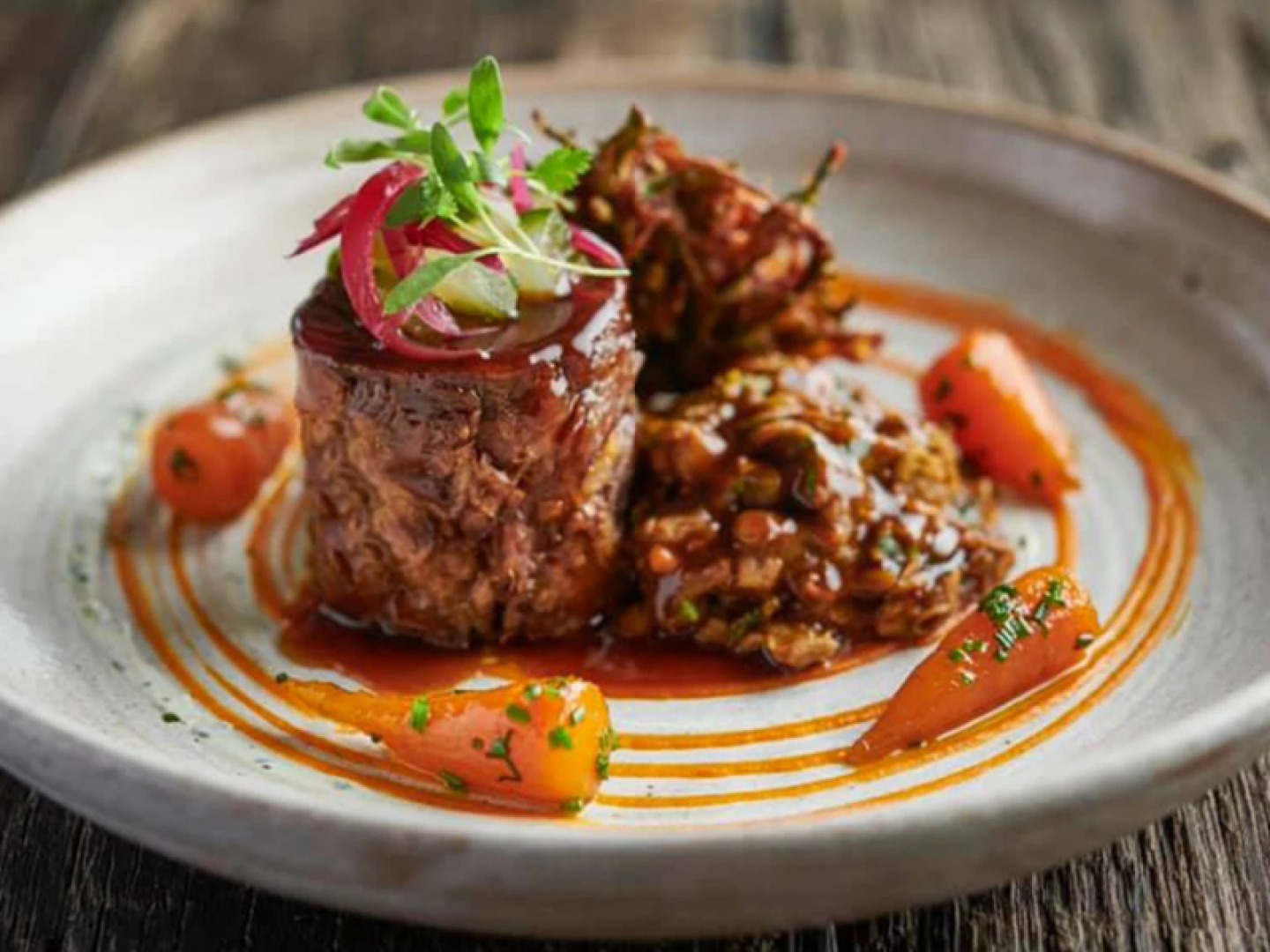 a plate of food. Steak sits high on the plate with four carrots surrounding it with a carrot puree around the outside
