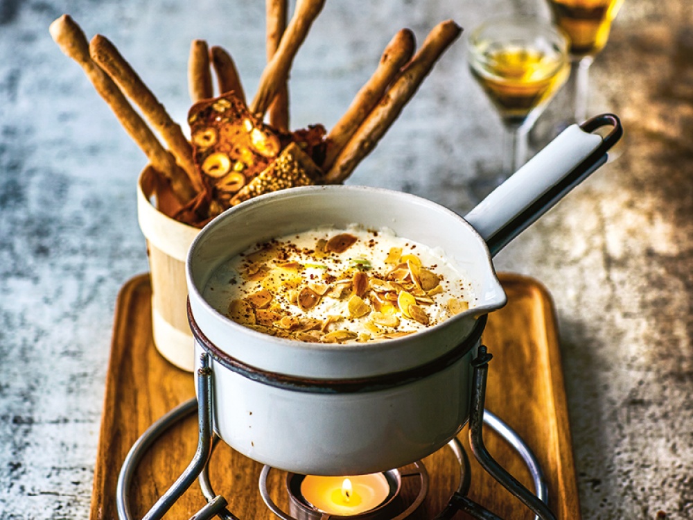 cheese fondue with toasted nuts on top with breadsticks