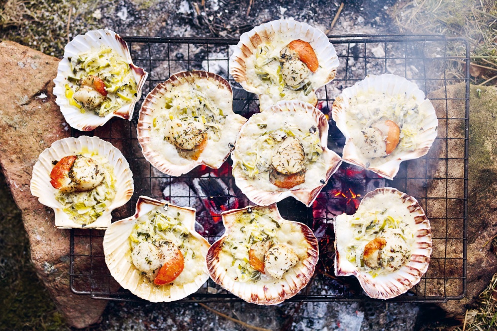 open scallop shell with scallops, and creamed leeks sitting on a barbecue