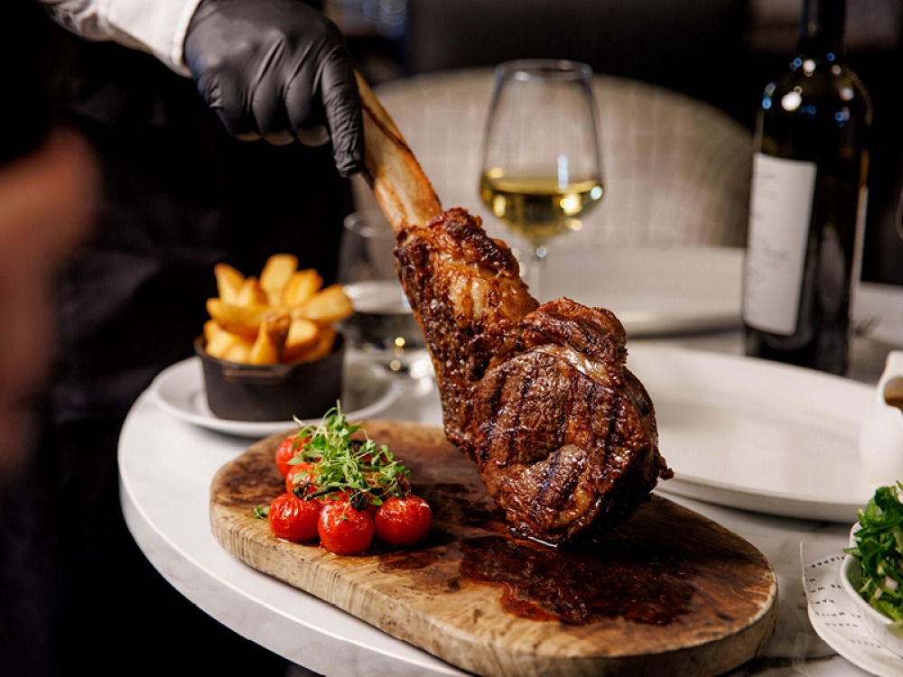 large pice of meat on the bone with cherry tomatoes and chunky chips