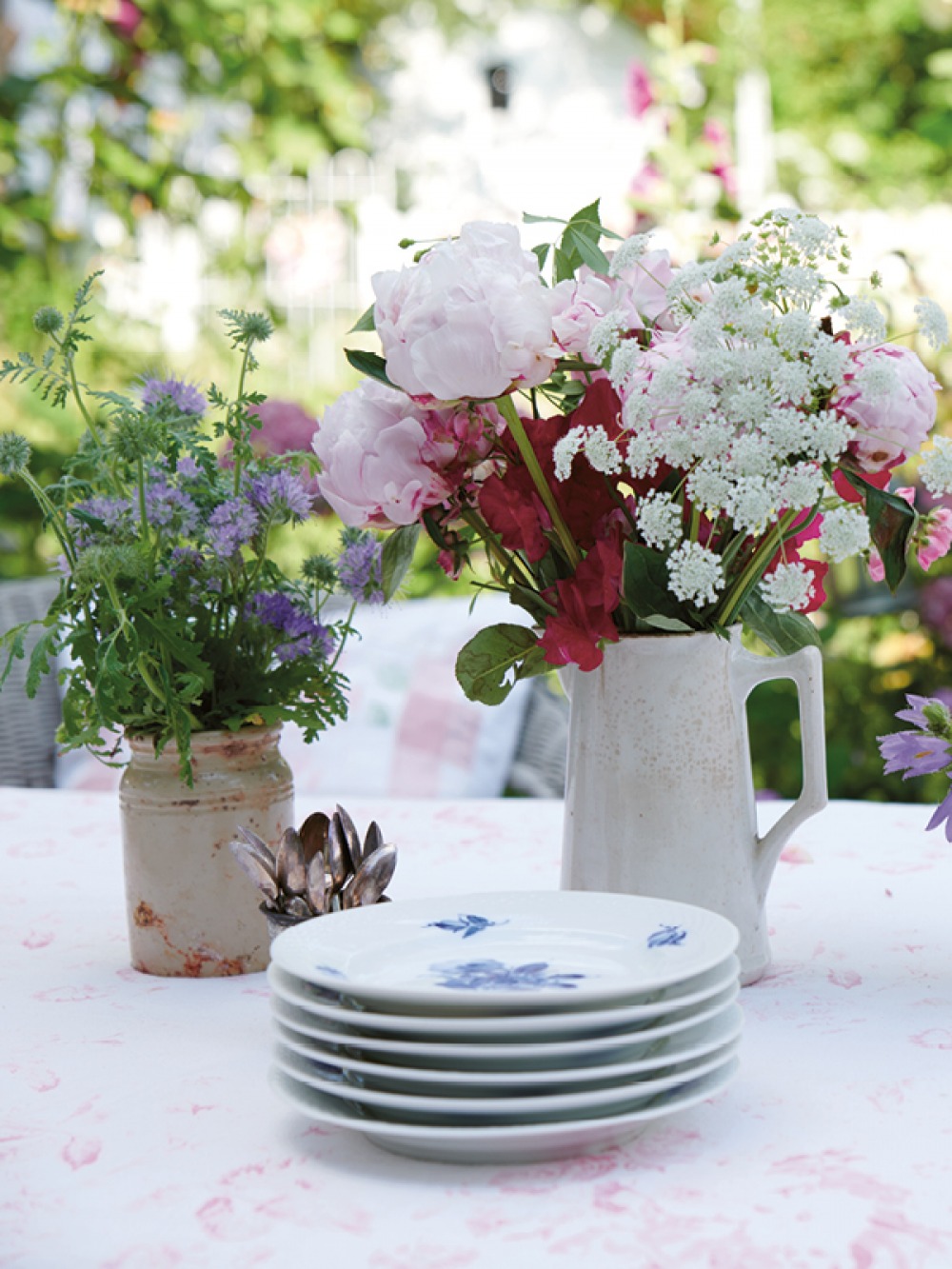 Plates, teaspoon and flowers in jars on an outdoor table