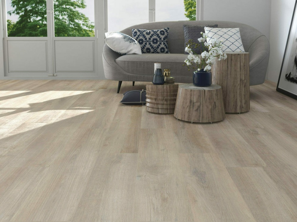 wood effect flooring with a grey sofa and 3 wooden tables decorated with flowers and vases