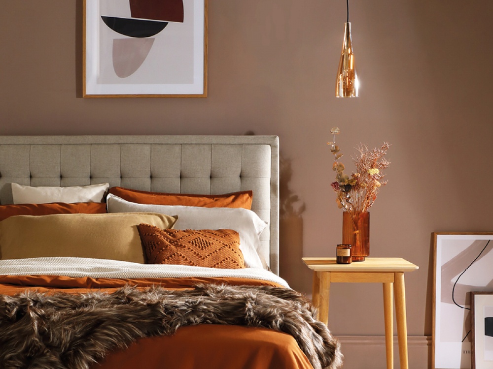 bed made up in bedroom which is paint and styled in brown tones