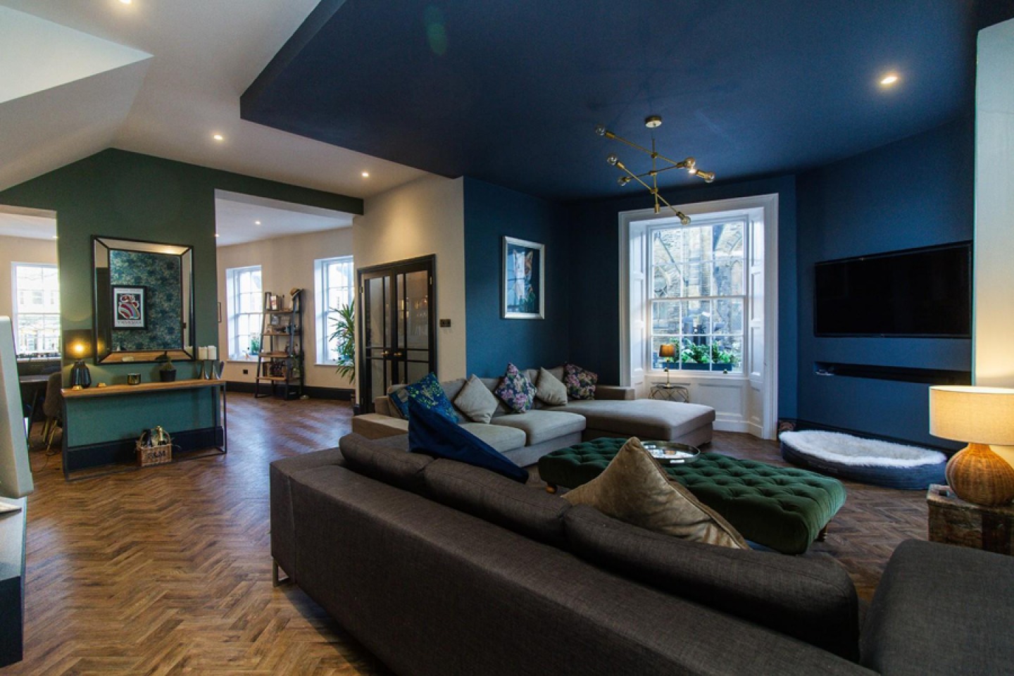 Large open plan lounge with parquet flooring, contemporary decor in dark blue and teal. Ambient lighting and modern accessories.