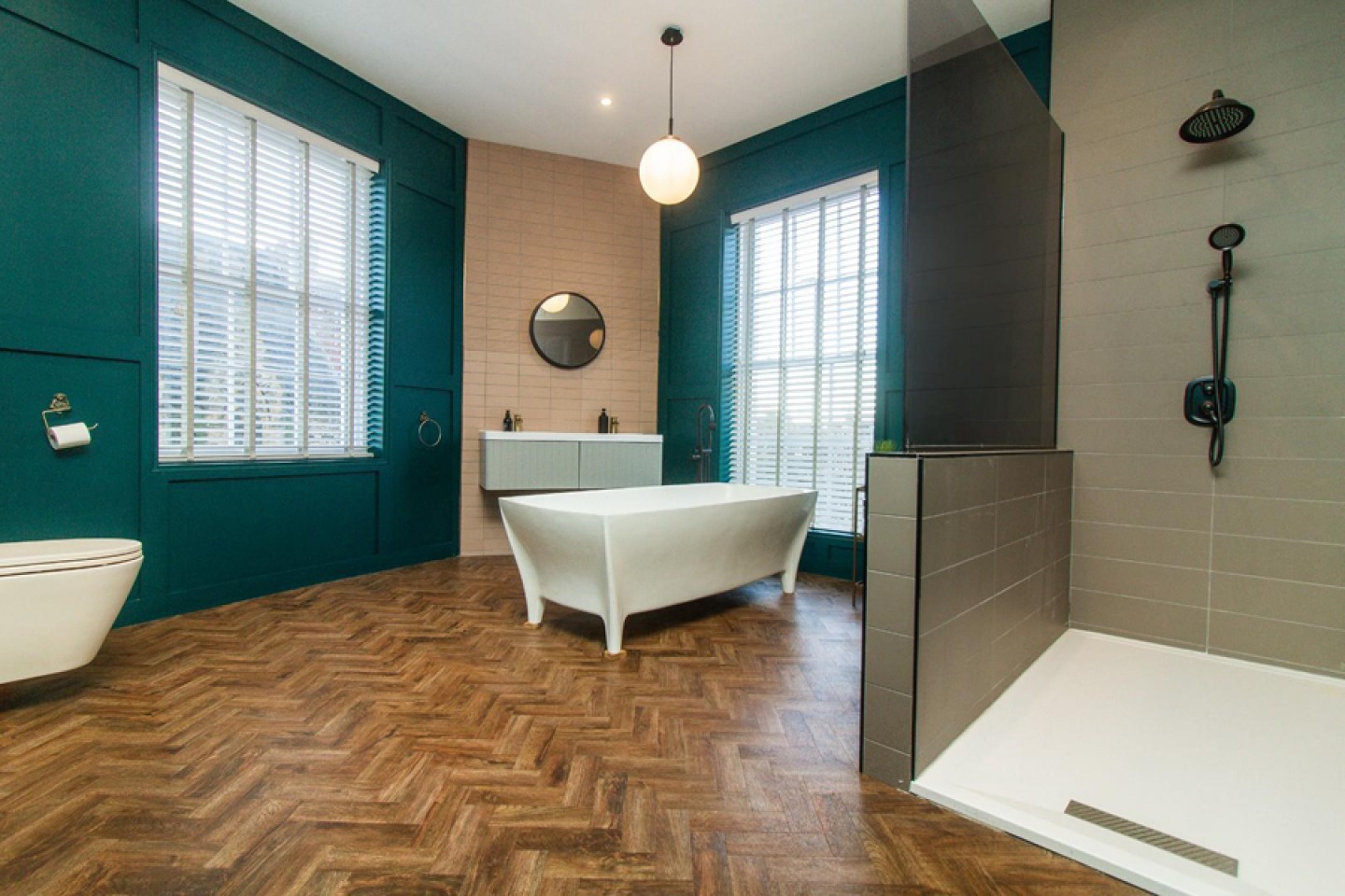 Contemporary bathroom with parquet wooden flooring, walk in shower, free standing bath, teal wood panelled walls large feature windows
