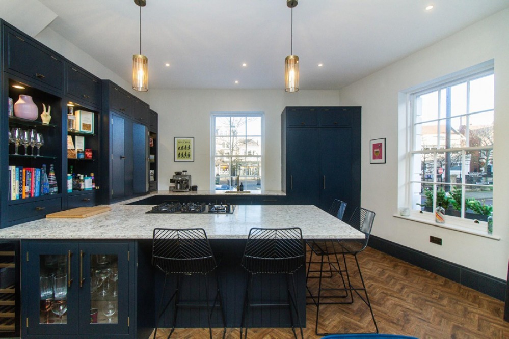 Contemporary open plan kitchen with dark blue cabinets, parquet wooden floor and glass pendants