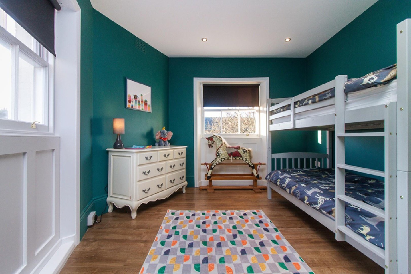 Childs bedroom with teal walls, white wooden sat windows, bunk beds and wooden flooring
