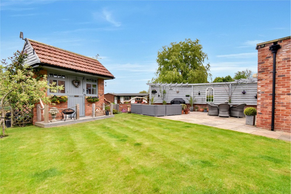 Lawned garden with patio area, grey fence and a brick summer house at the bottom