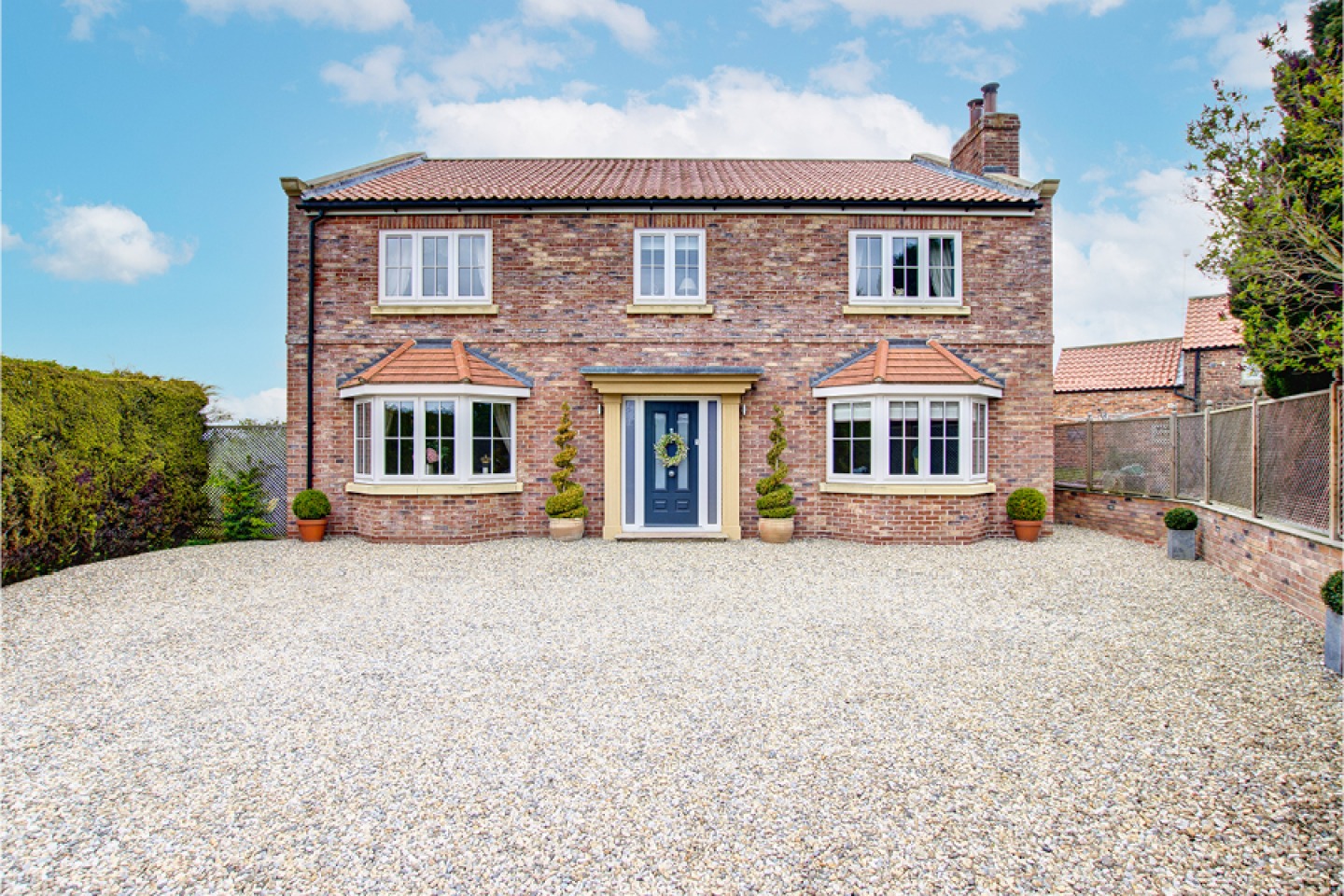 External shot of double fronted detached brick house with bay windows and gravelled drive
