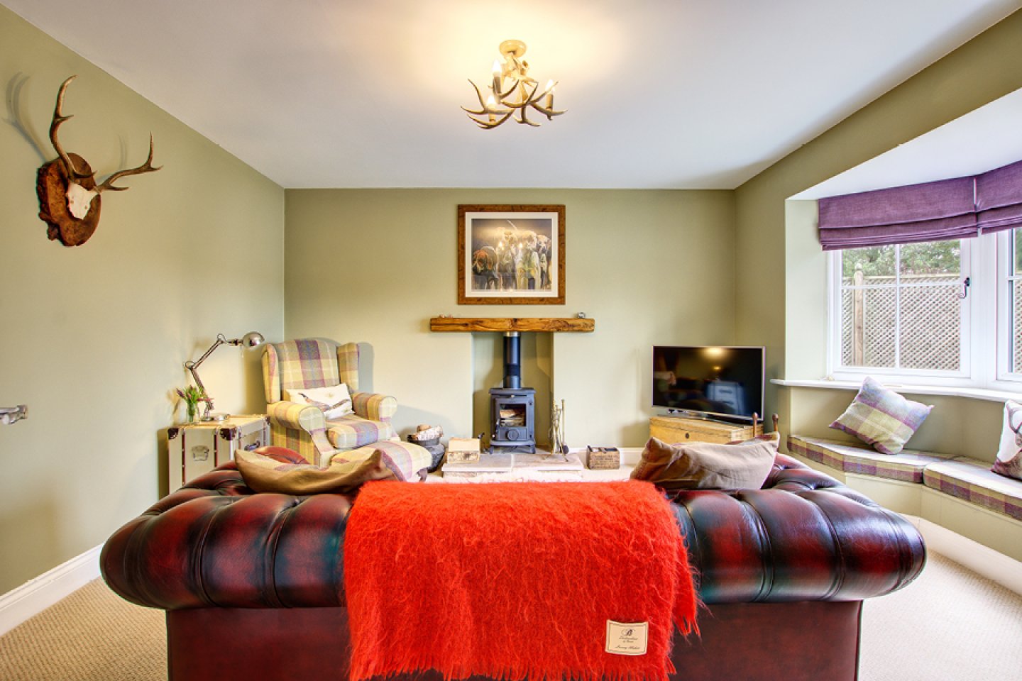 Cosy lounge with woodturning stove, leather Chesterfield and tartan armchair