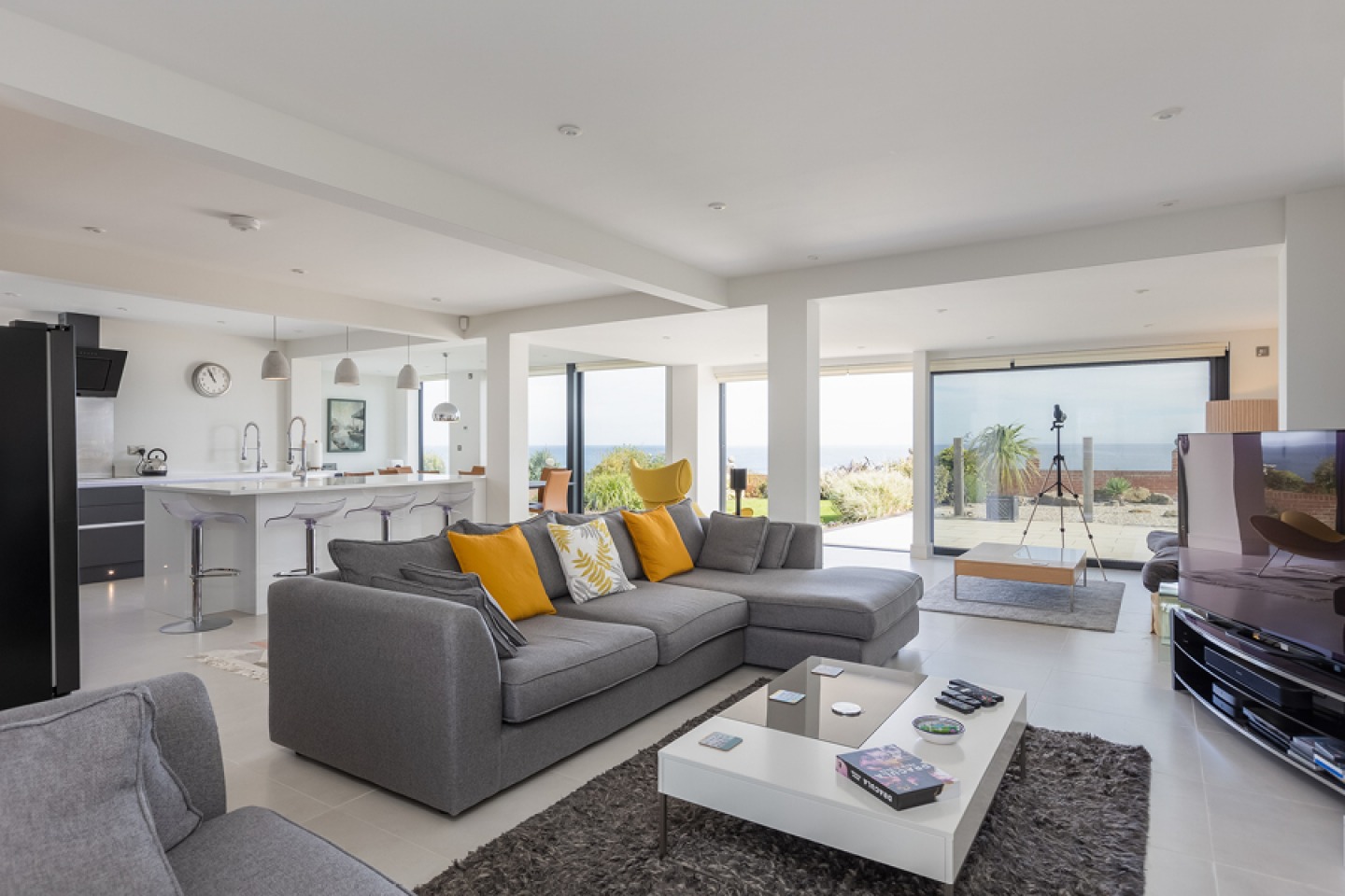 Large, modern open plan kitchen and living area. floor to ceiling glass door with views out to sea.