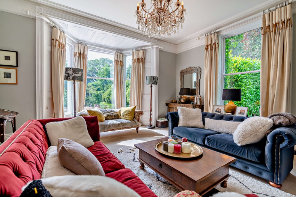 Large lounge with period features tall windows and colourful velvet Chesterfield sofas