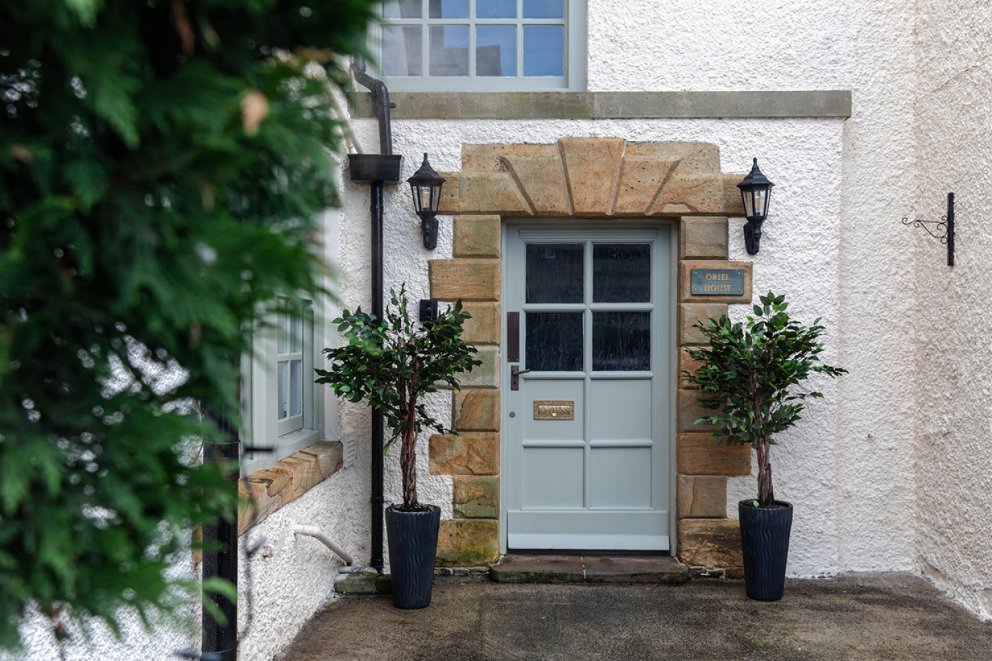 Front door of Oriel House a stonework surround and two potted Bay trees and wall lanterns