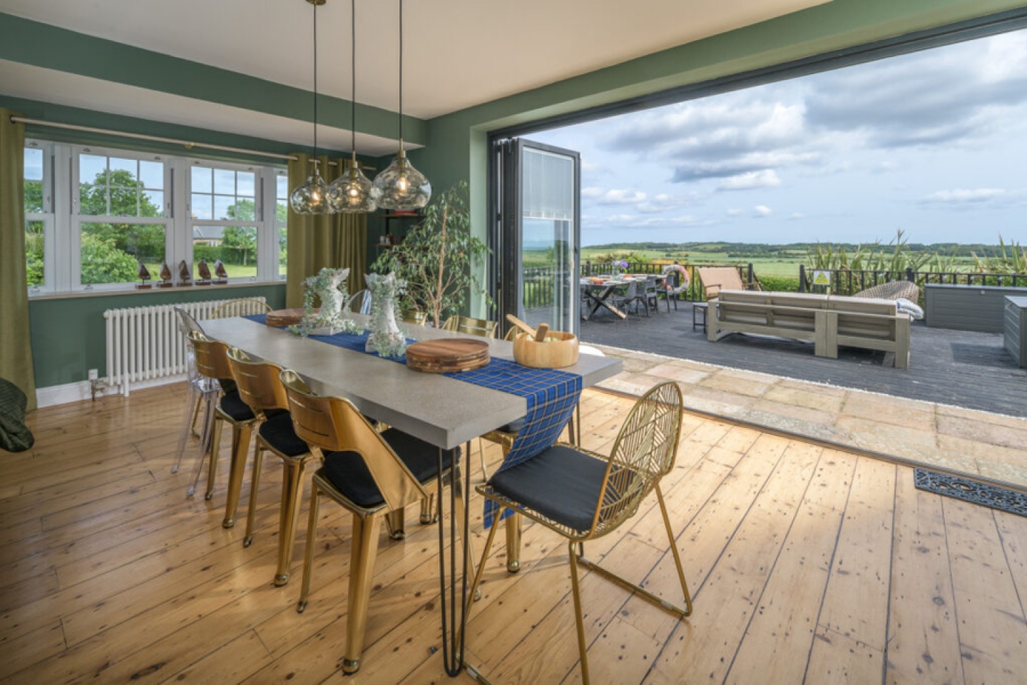 Large dining table looking over bi-folding doors to a decked area