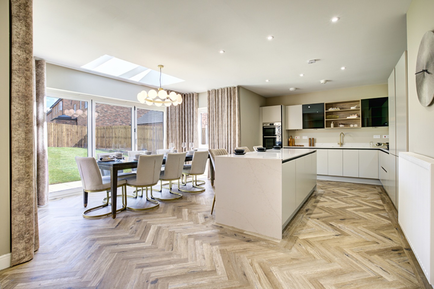 Modern high gloss white kitchen with open plan dining looking onto bifold door leading to garden