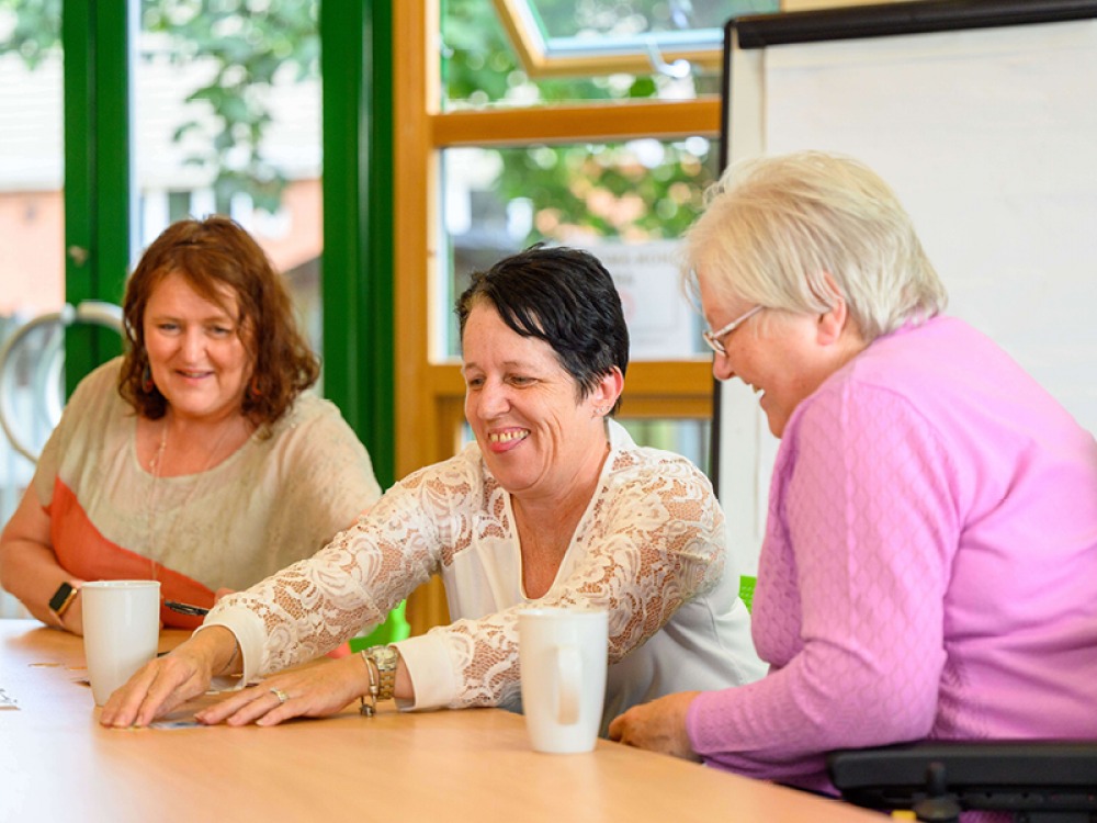 three people sat around a table having a laugh whilst at speech therapy