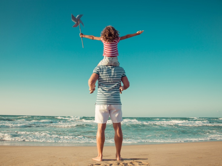 child on a mans shoulders standing on a beach looking out to see