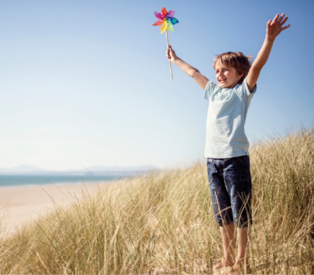 child holding arms up with a rainbow windmill on a sand dune