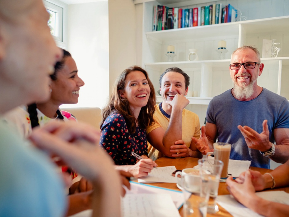 Group of people sitting around a table chatting with teas and coffees