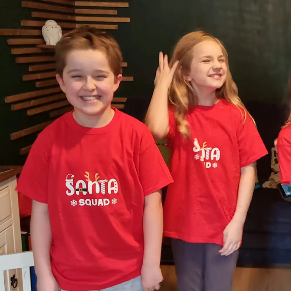 Boy and girl smiling wearing red Santa Squad T-shirts