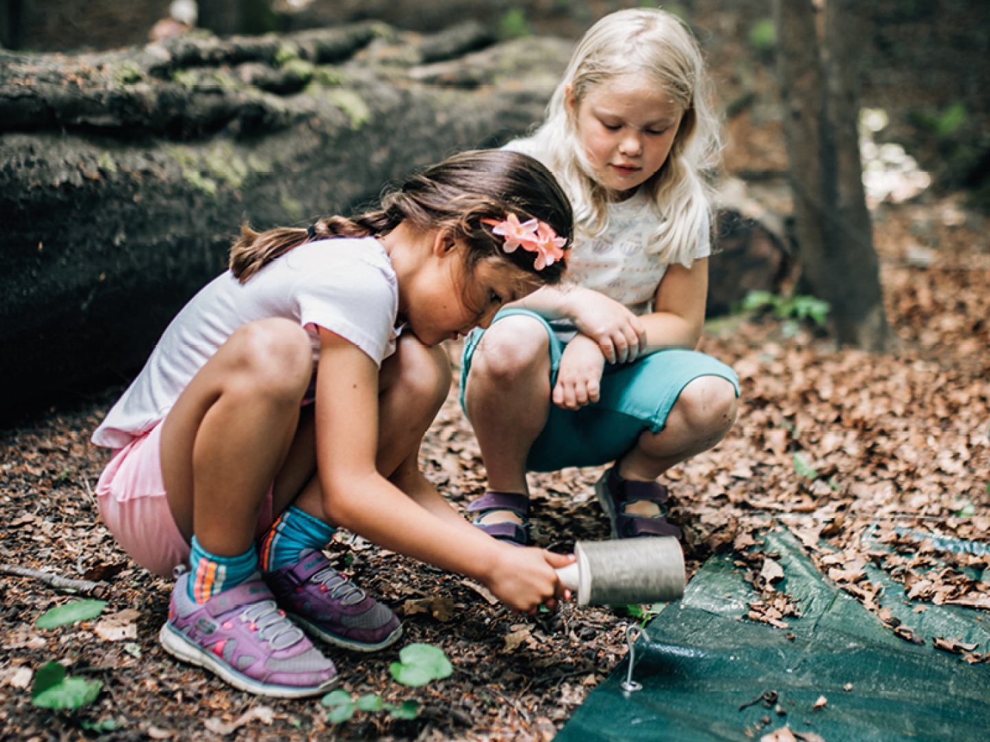2 young girls banging tent pegs into the ground