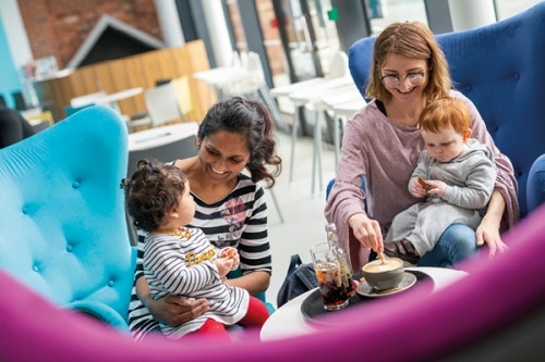 two mums with babies on their laps having drinks