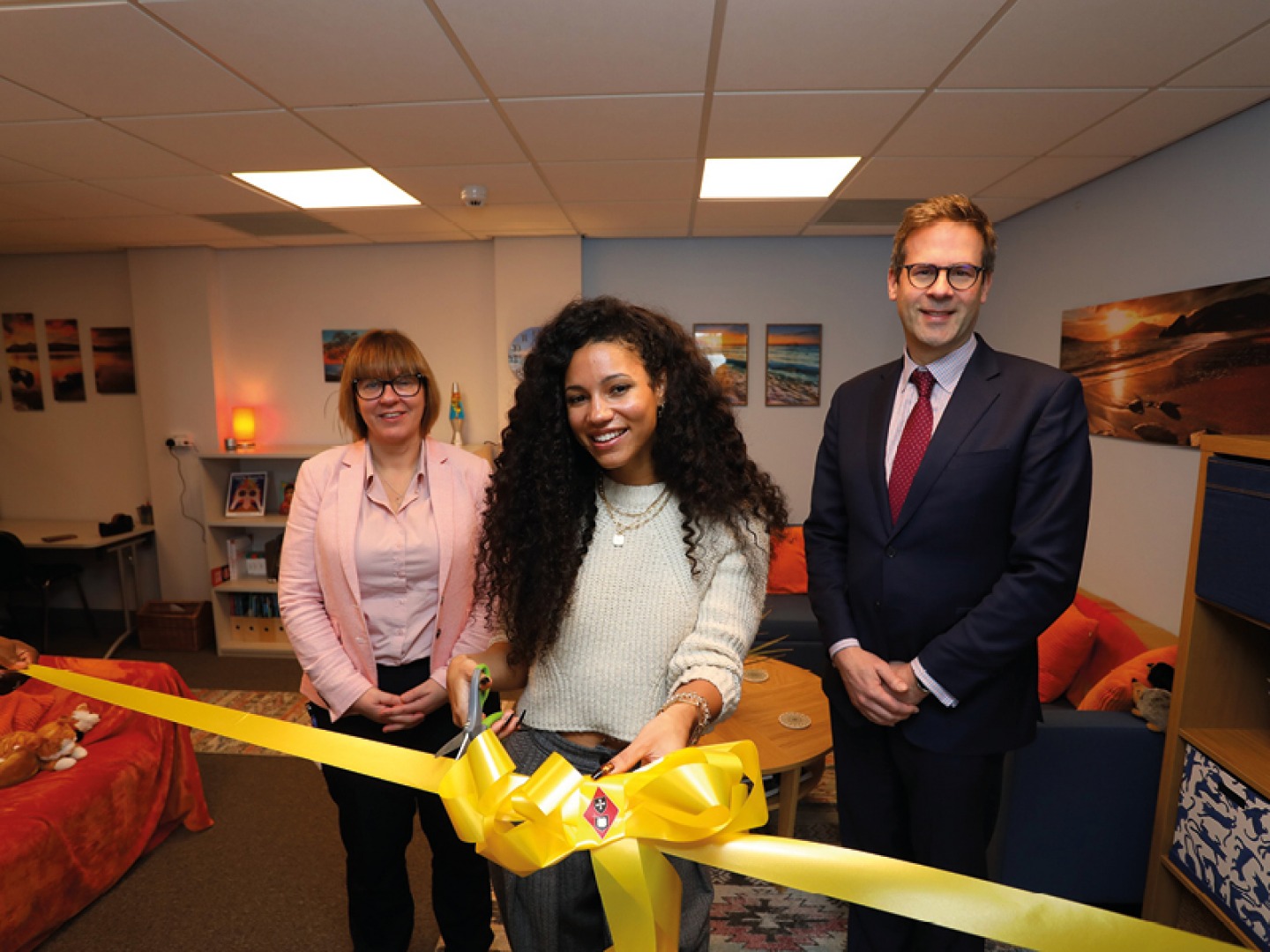 2 women and a man standing together cutting a yellow ribbon