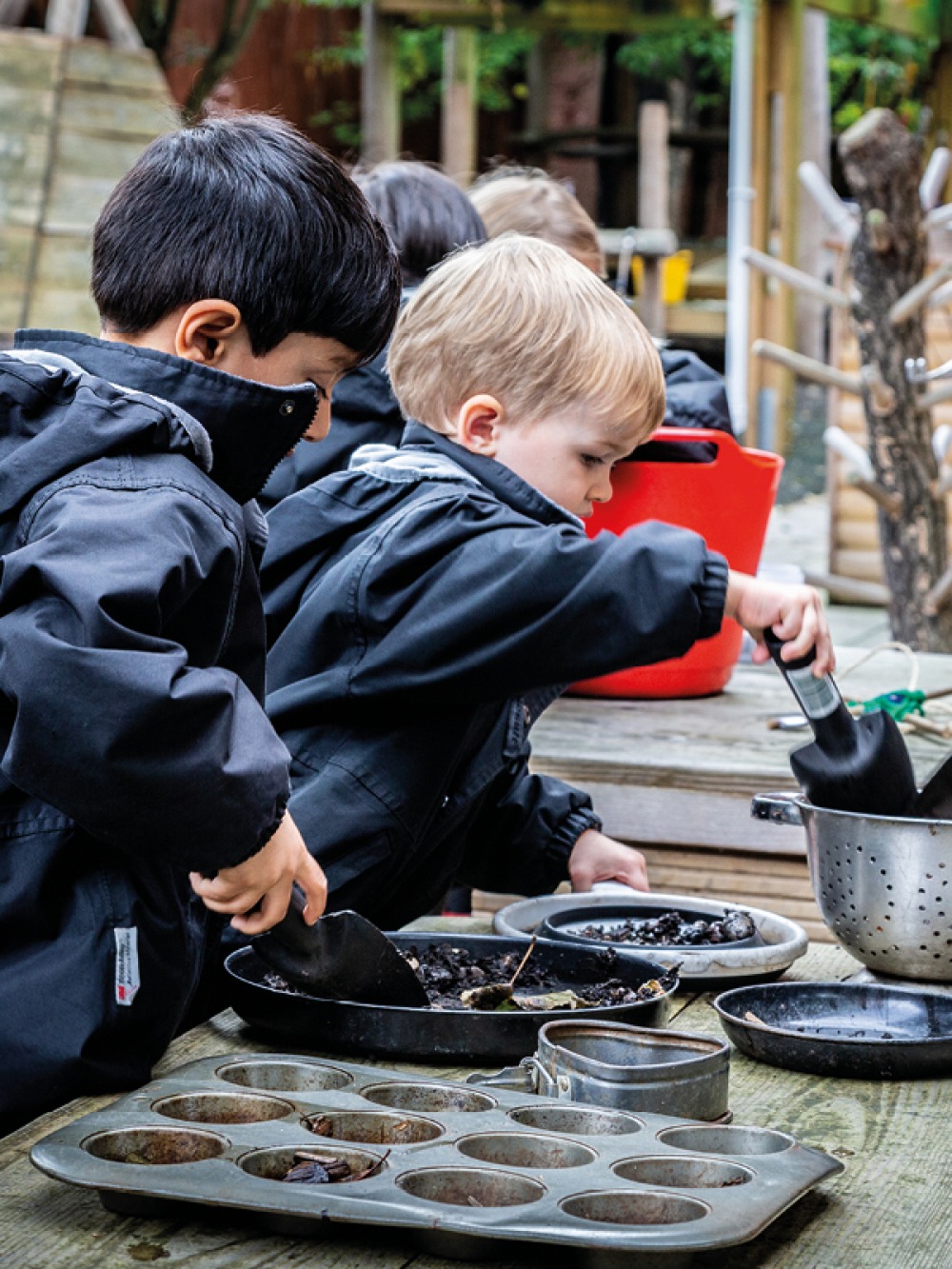 2 young children playing outdoors with soil and cooking utensils