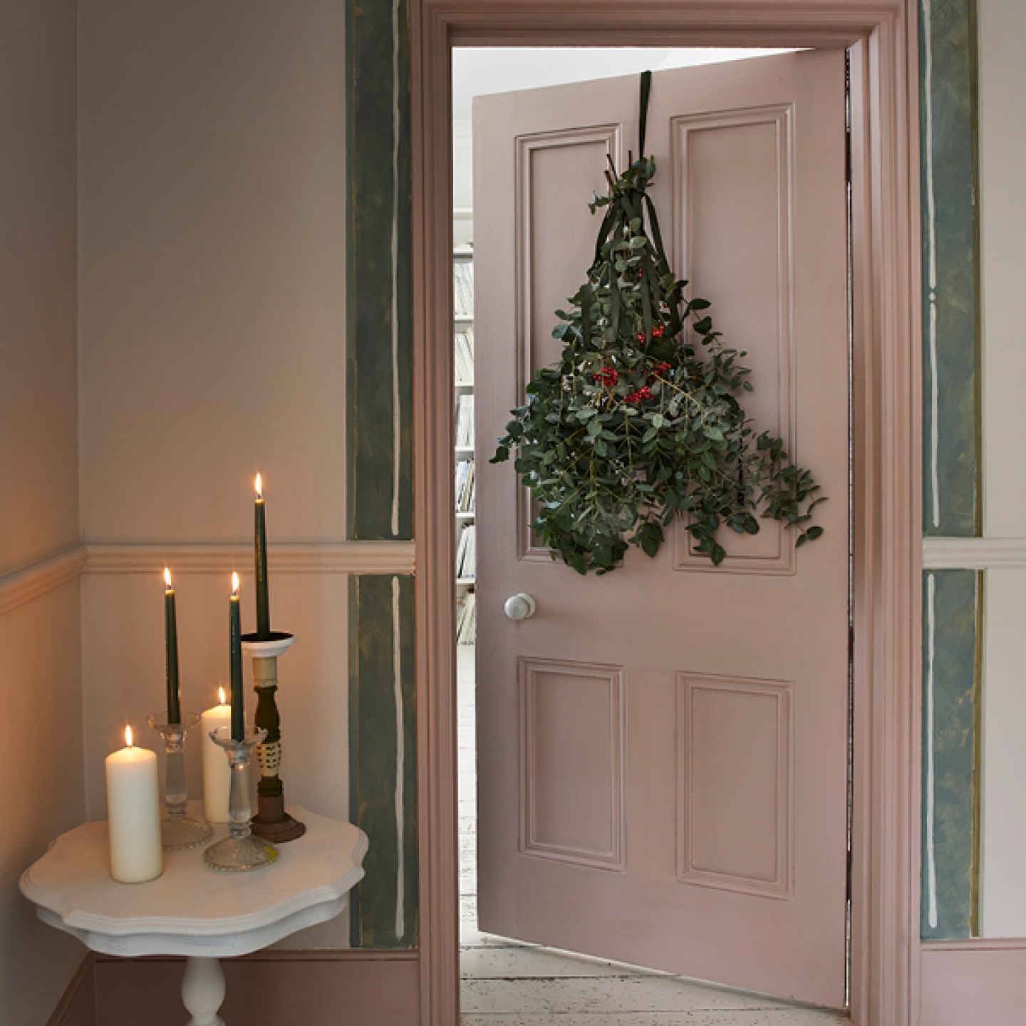 internal pink door with hanging wreath and candles in side table