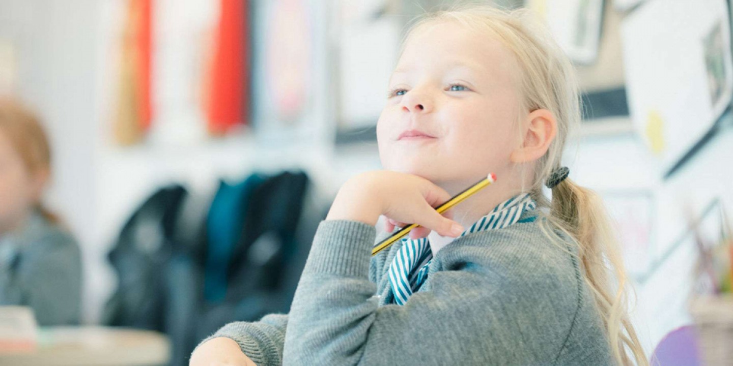 Young pupil smiling in class resting her chin on her hand