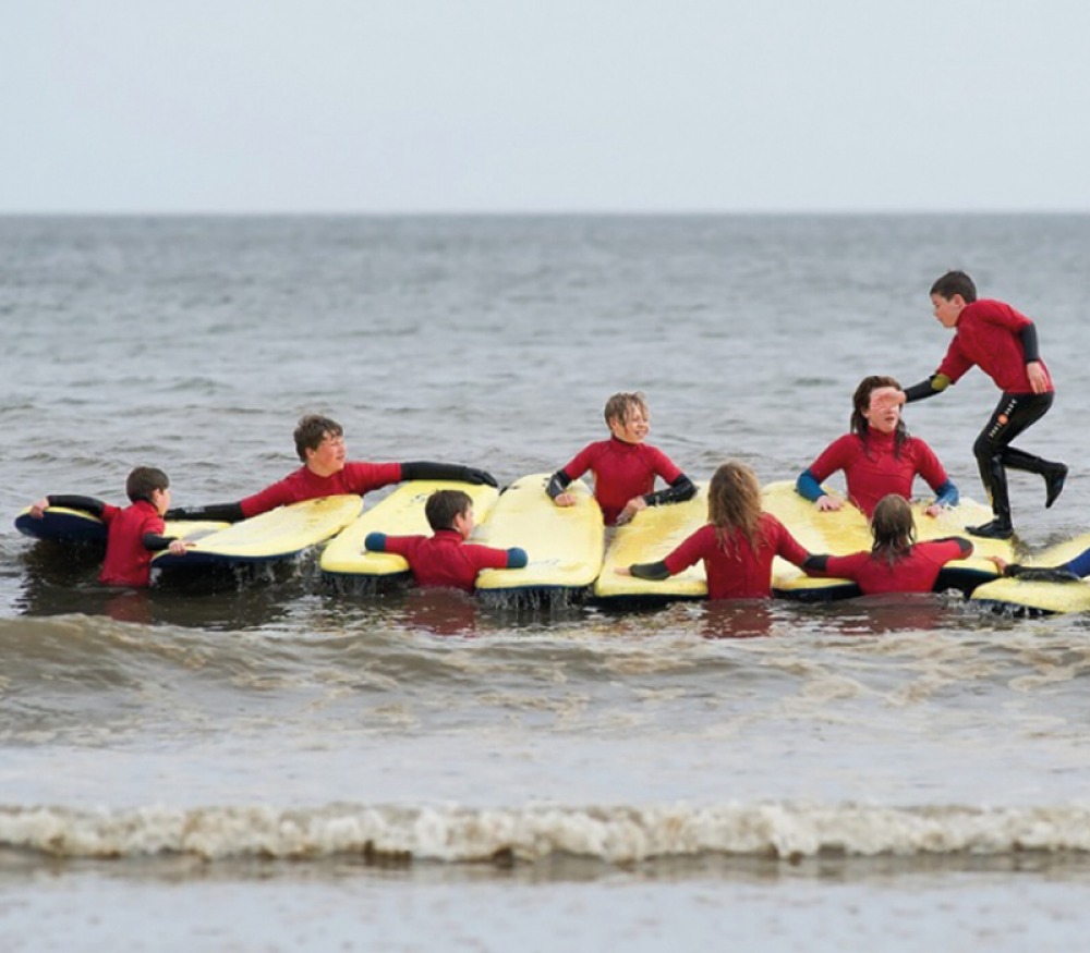 children holding surf boards together as a bridge for another to run across