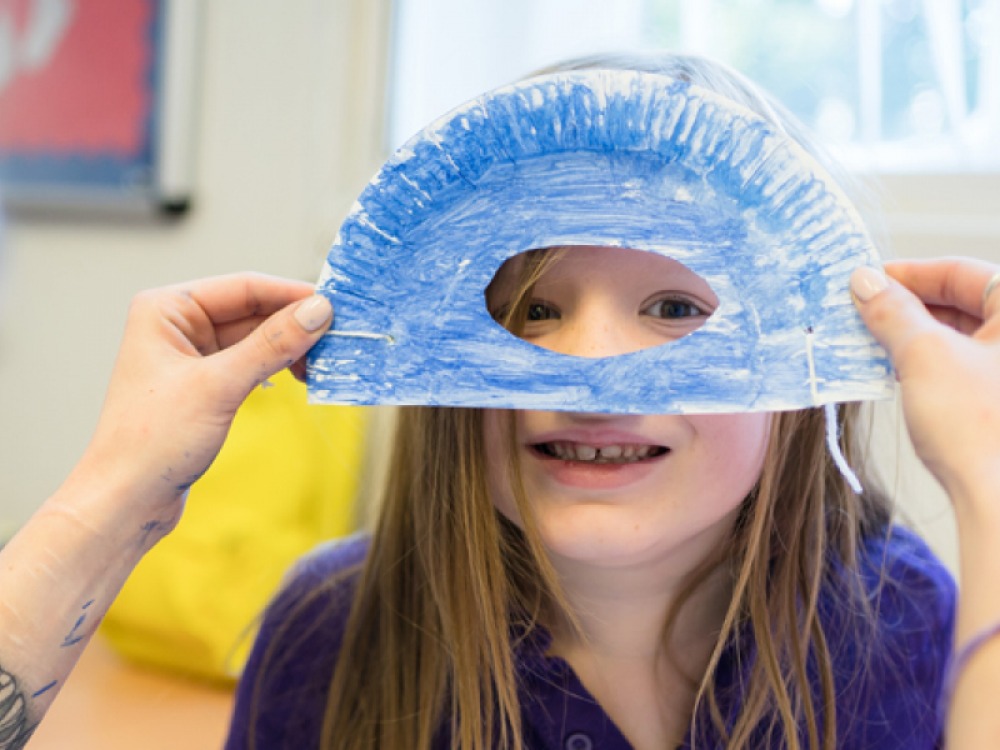 hands holding a home-made mask up to a (smiling) young girls face