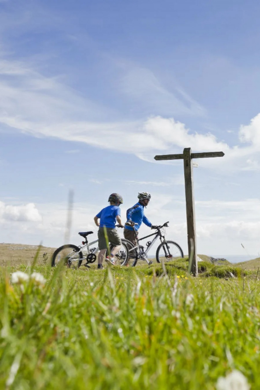 father and child with their bikes at a wooden signpost surround by fields and rolling hills | Malham Tarrn