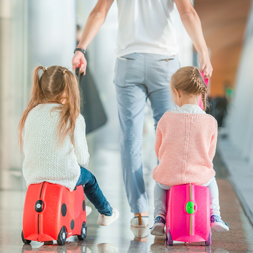 children being pulled along on cases at airport