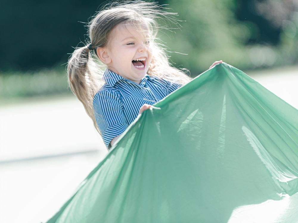 young student lifting a green sheet laughing